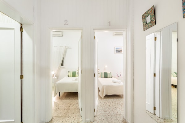 A hallway leading to two bedrooms, each with a bed, bedside table, and a mirror.