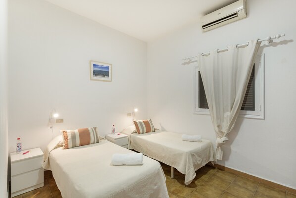 Ein Hotelzimmer mit zwei Betten, einem Nachttisch, einer Wandklimaanlage, einem Fenster mit Vorhängen und einem kleinen Bild an der Wand.