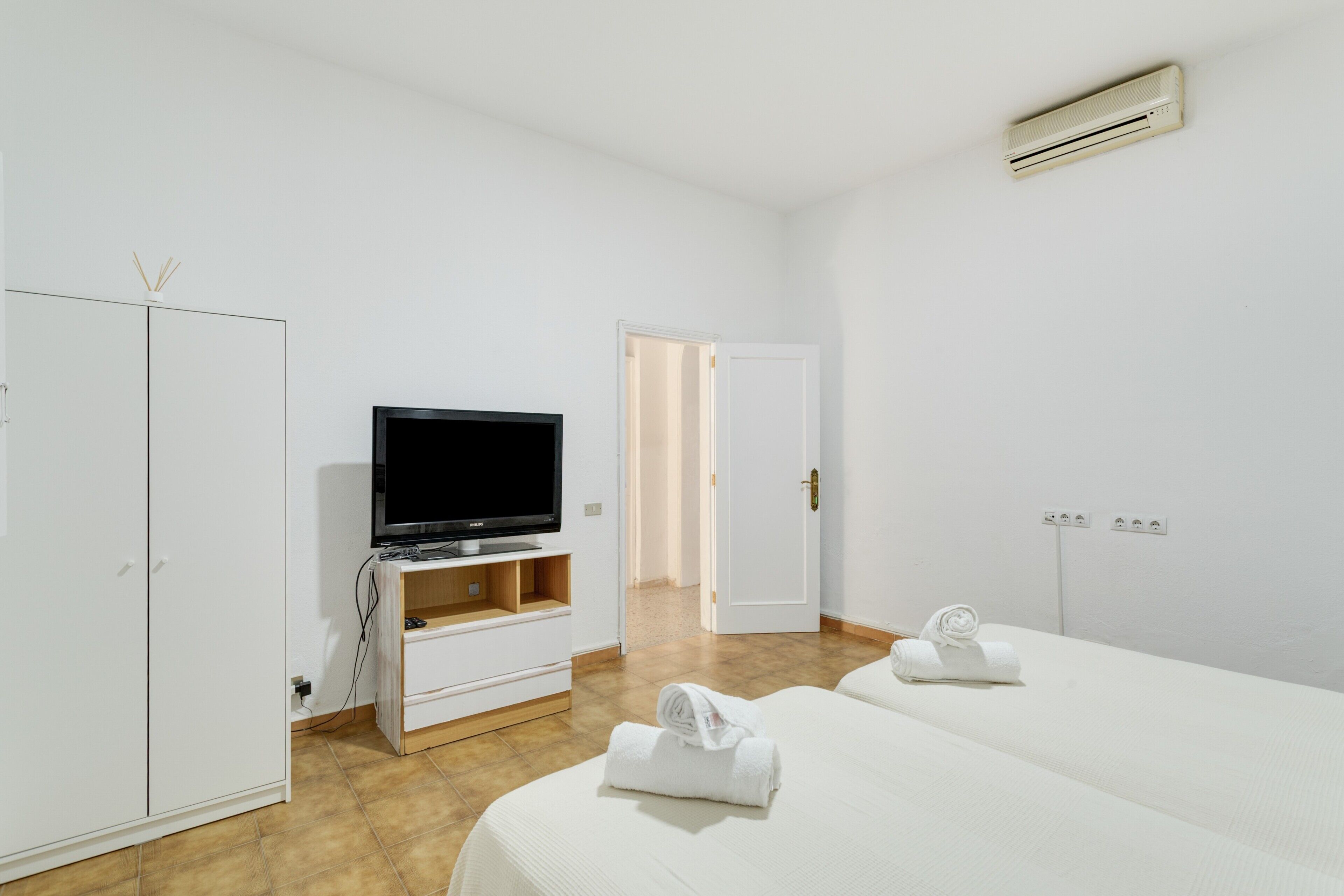Habitación de hotel con televisión, armario, dos camas y puerta al baño.