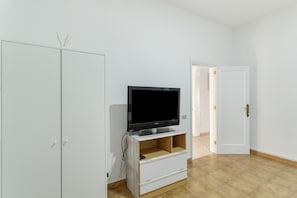 Una habitación con televisión sobre un mueble de madera, un armario y una puerta que da a otra estancia.