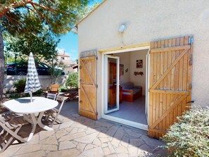 A patio with a table and chairs, a wooden gate, and a bed inside a room. - Bright house for 6 with pool near Sète (Vic-la-Gardiole)