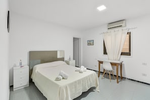 Ein Schlafzimmer mit Bett, Nachttisch, Schreibtisch, Stuhl und Klimaanlage.
