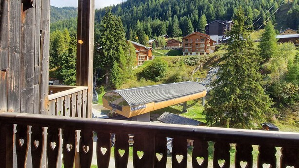 A wooden balcony with heart-shaped cutouts, overlooking a mountainous area with buildings and trees. - Studio with Cabin in Valfréjus - Pets Allowed (Valfréjus)