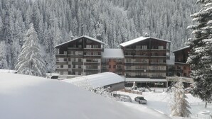 A multi-story hotel with balconies, surrounded by snow-covered trees and a mountainous backdrop. - Studio with Cabin in Valfréjus - Pets Allowed (Valfréjus)