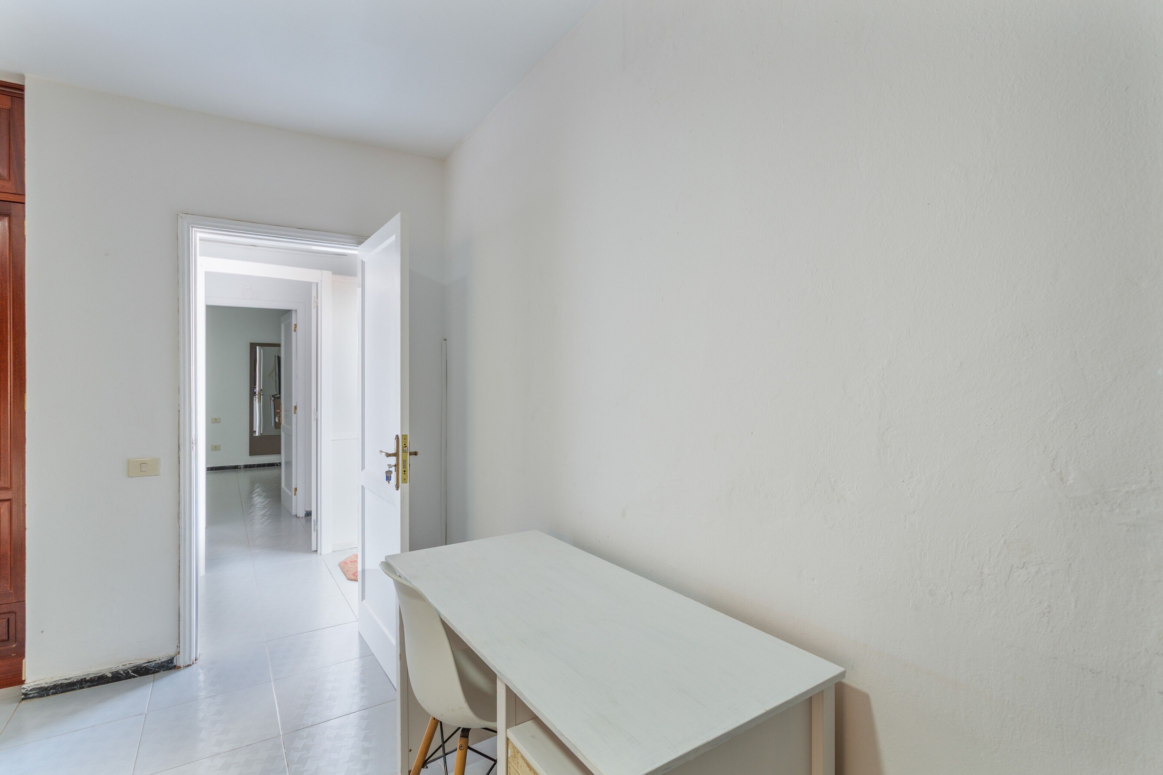 A room with a white desk, a chair, and a door leading to another room.