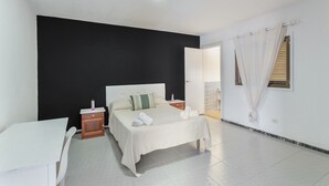 A bedroom with a bed, bedside tables, a nightstand, a window with curtains, and a door leading to another room. - Exterior Double Room (Arinaga)
