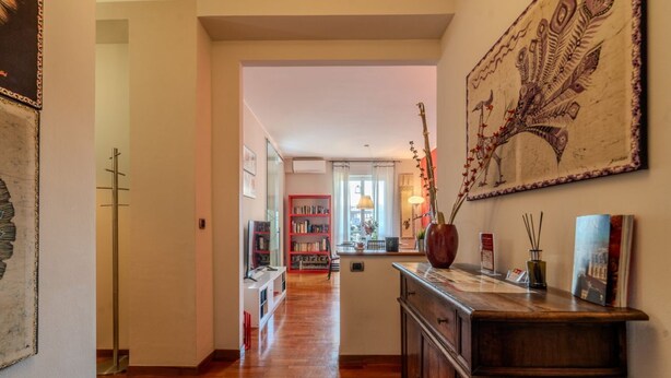 A hallway with wooden flooring, a red bookshelf, a decorative vase, and a wall-mounted artwork.