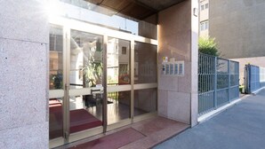 A building entrance with glass doors, a metal fence, and a red mat outside.