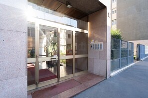 A building entrance with glass doors, a metal fence, and a red mat outside.
