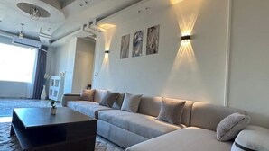A modern living room with a large beige sofa, a dark coffee table, and wall-mounted lighting. - Cheops Horizon Pyramids View (Giza Governorate)