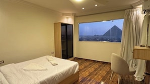A hotel room with a bed, a chair, a window with a view of a mountain, and a wooden floor. - Cheops Horizon Pyramids View (Giza Governorate)