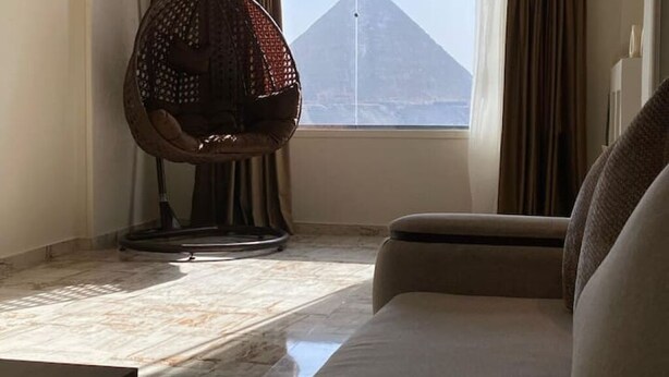 A room with a view of a pyramid, a hanging chair, and a sofa. - Cheops Horizon Pyramids View (Giza Governorate)