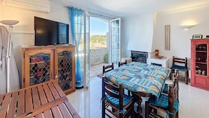 Uma área de refeições com mesa e cadeiras, uma televisão sobre um móvel, uma lareira e uma vista através de uma porta de vidro.