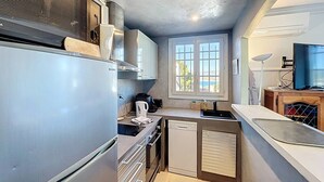 Cozinha compacta com geladeira, fogão e lava-louças. Uma janela oferece iluminação natural e vista para o exterior.