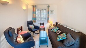 Sala de estar com sofá, duas poltronas, mesa de centro e janela com cortinas.