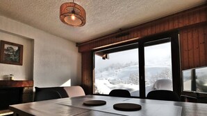 Zona pranzo con un tavolo grande, sedie, una lampada a sospensione e vista su un paesaggio innevato attraverso ampie finestre.