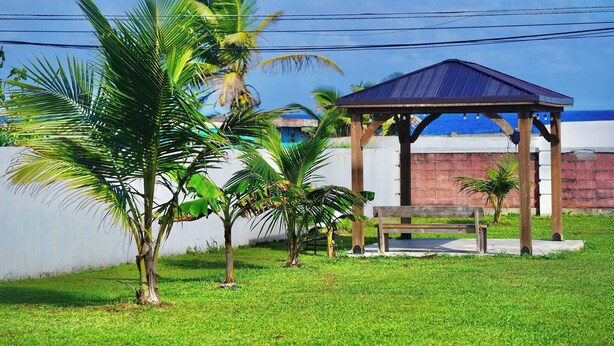 A gazebo with a wooden bench, surrounded by palm trees and a grassy area. - Room-mar Azul - Ocean View Private Studi (Arecibo)