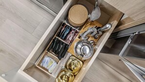 Eine Küchenschublade mit verschiedenen Küchenutensilien, einem Topf und einem Sieb.