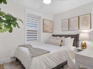 Un dormitorio con cama, mesitas de noche, lámpara y cuadros en la pared.