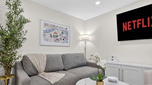 Ein modernes Wohnzimmer mit einem grauen Sofa, einem runden Couchtisch, einem Wand-Fernseher und einer gerahmten Karte.