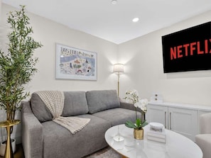 Una sala de estar moderna con un sofá gris, una mesa de centro redonda, un televisor montado en la pared y un mapa enmarcado.