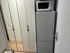 Eine Küche mit einem weißen Kühlschrank und einer Mikrowelle, einer Tür mit Griff sowie einem Lichtschalter.