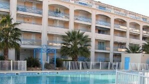 Un hotel de varios pisos con un área de piscina, que incluye una piscina azul y una cerca blanca alrededor.