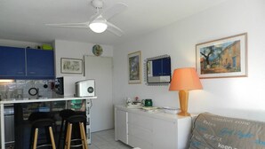 Un espacio habitable compacto con kitchenette, comedor y sofá con cojín estampado.