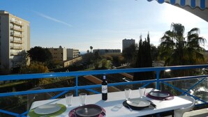 Mesa lista para cenar con una botella de vino, copas y platos, con vista a un paisaje urbano con edificios y palmeras.