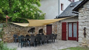 Un edificio de piedra con patio, mesas al aire libre y una toldo colgante.