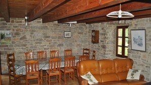 Un comedor con pared de piedra, vigas de madera en el techo, una mesa con sillas y un sofá de cuero.