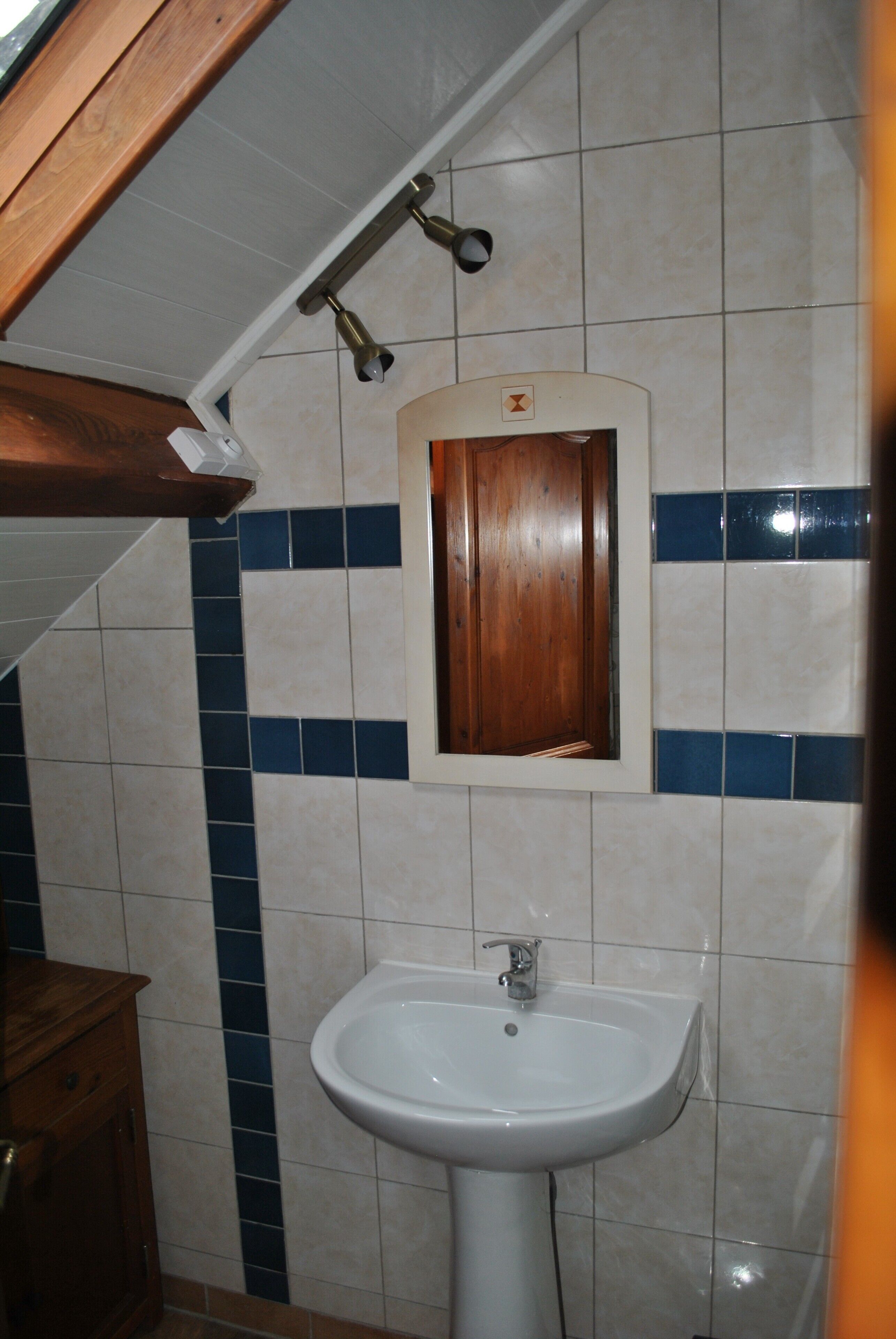 Een badkamer met een wit wastafel, een houten kastje en een spiegel met houten lijst.