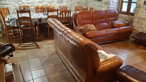 Una sala de estar con pared de piedra, un sofá de cuero marrón, una mesa de comedor con sillas y un reloj en la pared.
