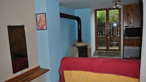 A room with a bed, a wooden bench, a TV, and a window with a view of greenery. - Gîte “Le Vignou” in Ste-Enimie: Mountain View, Private Terrace, and Wi-Fi (Gorges du Tarn Causses)