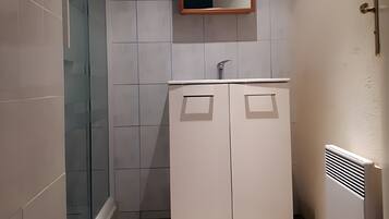 Une salle de bain avec une douche à parois de verre, un lavabo blanc avec un miroir au-dessus, et un radiateur fixé au mur.