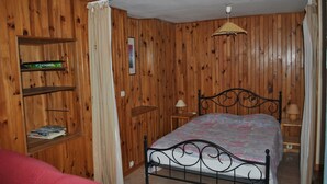 A bedroom with wooden paneling, a metal bed frame, a bedside table with a lamp, and a shelf with books. - Gîte “Le Vignou” in Ste-Enimie: Mountain View, Private Terrace, and Wi-Fi (Gorges du Tarn Causses)