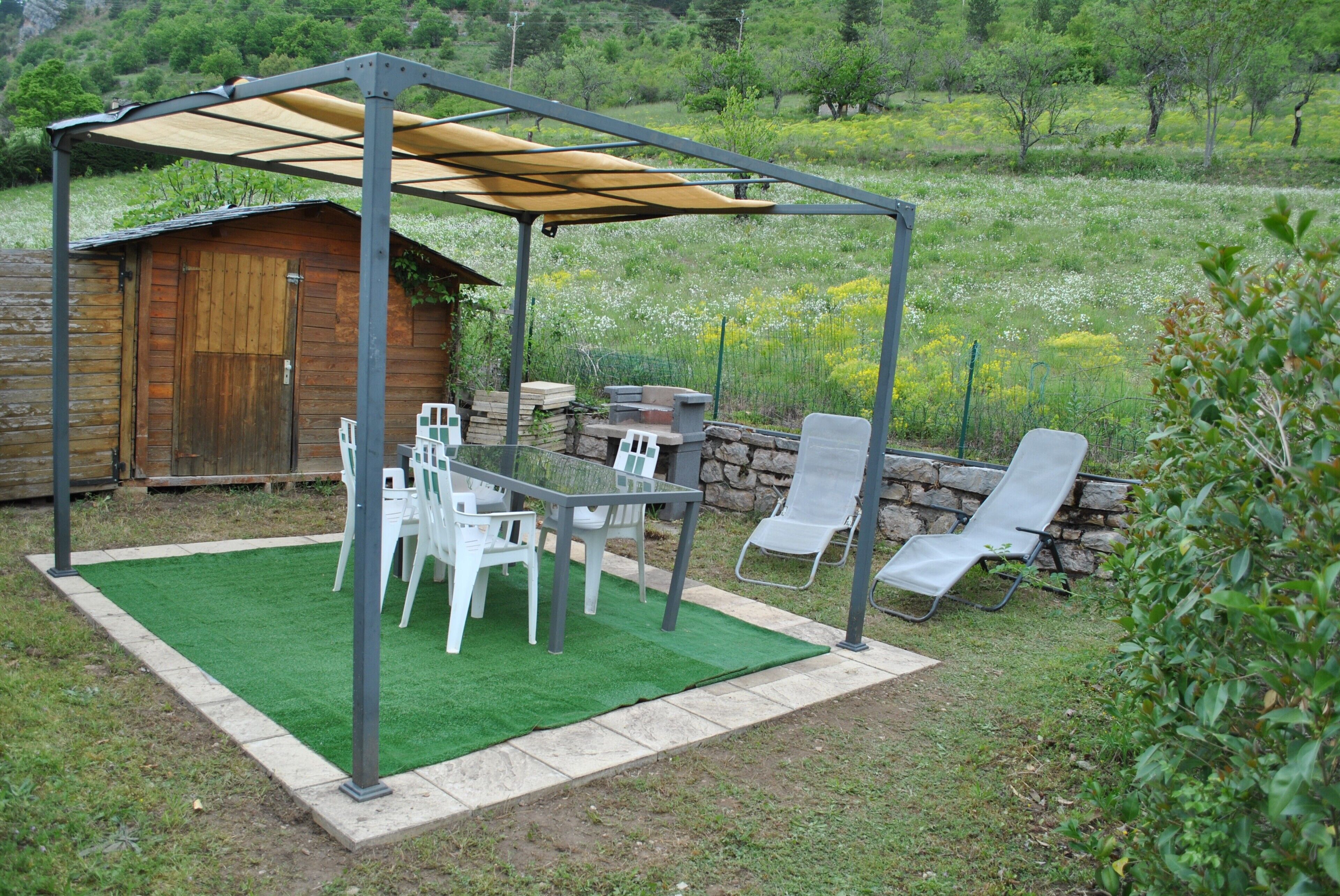 A covered patio with a table and chairs, a wooden shed, and a stone wall.