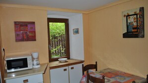 A compact kitchen with a microwave, coffee maker, and a window with a view of greenery. - Gîte “Le Vignou” in Ste-Enimie: Mountain View, Private Terrace, and Wi-Fi (Gorges du Tarn Causses)