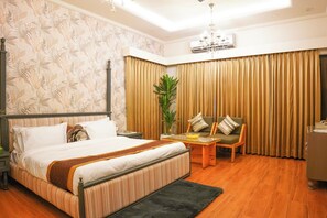 Ein Hotelzimmer mit einem großen Bett, einem Holztischchen, einem Sessel und einem Blumentopf.