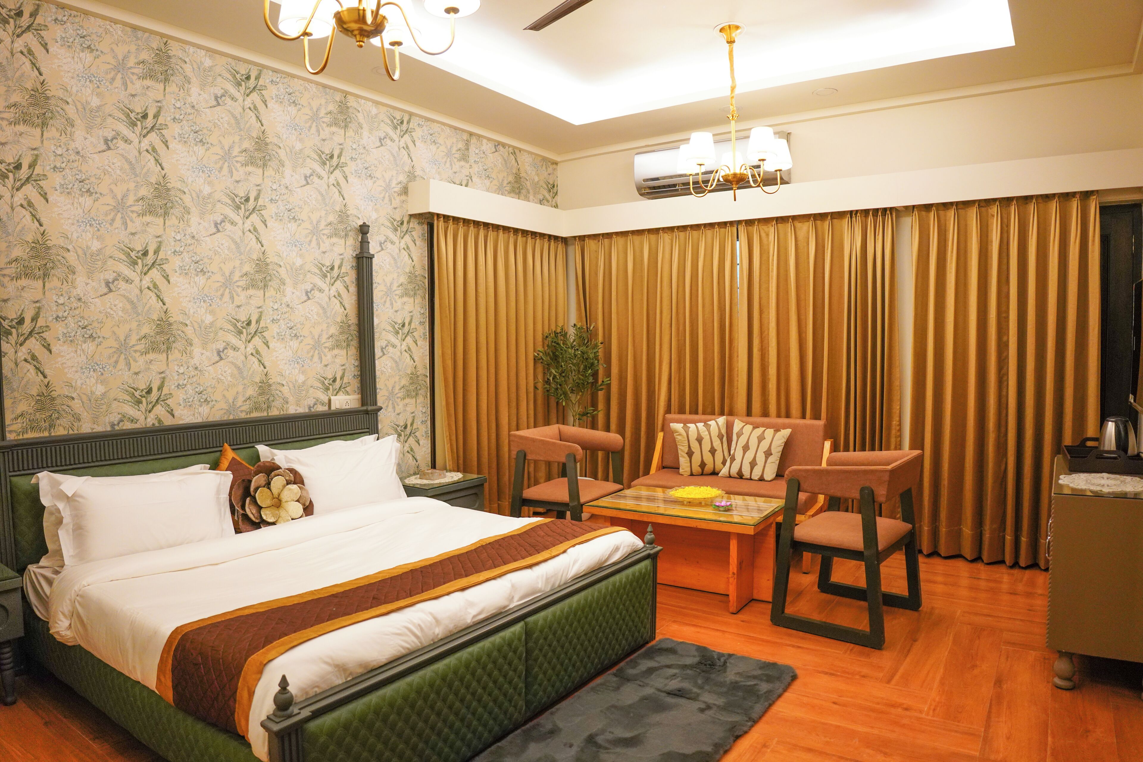 A hotel room with a bed, two chairs, a table, and a plant.
