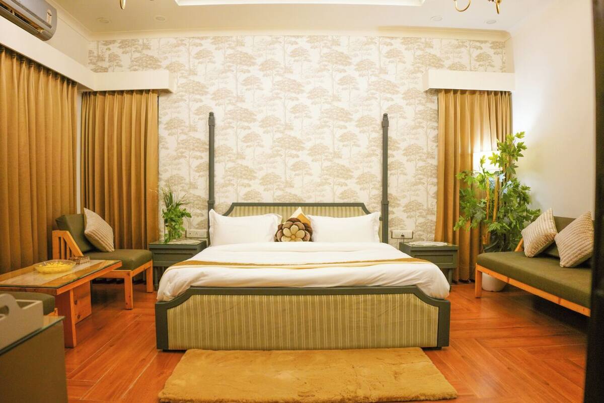 A bedroom with a large bed, two bedside tables, a green sofa, a wooden bench, and a small table with a plant.