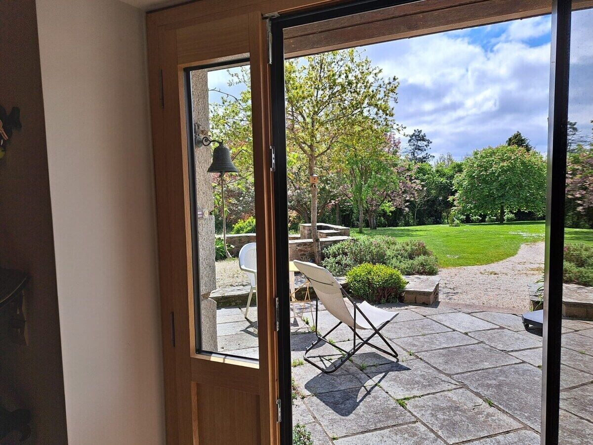 Blick durch eine Glastür auf eine Terrasse mit Rasen, Steinplatten und Gartenmöbeln.
