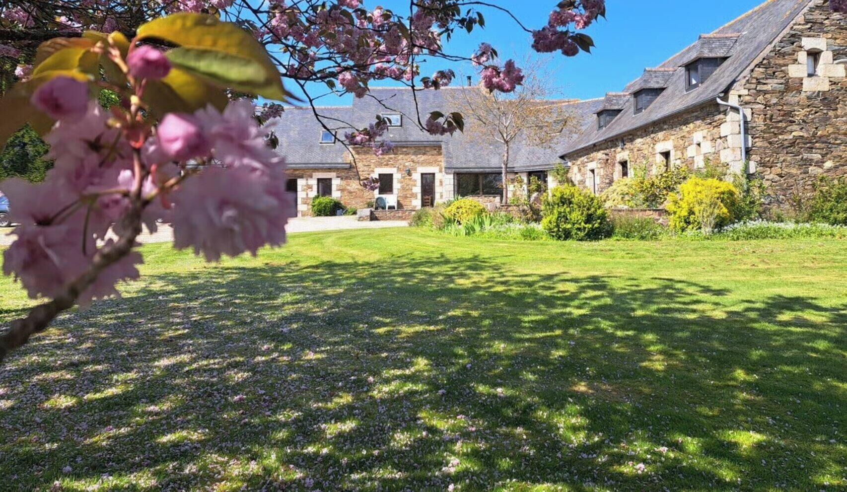 Ein Steinhaus mit geneigtem Dach, einem gepflegten Rasen und blühenden Pflanzen.