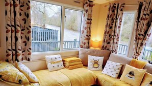 Ein gemütliches Zimmer mit Sofagarnitur, einem Fenster mit Vorhängen und einer Lampe.