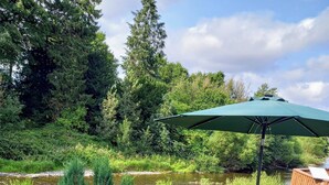 Eine Terrasse mit Gartenmöbeln, Blick auf einen Fluss und ein Geländer aus Holz.