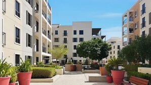 A courtyard with potted plants, a bench, and modern buildings with balconies. - Stylish 2BR with Beach Access (Dubai)