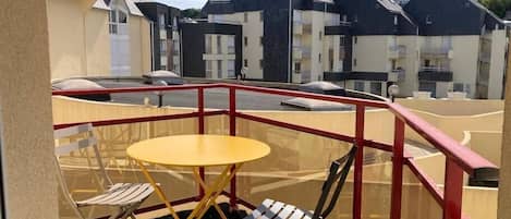 A balcony with a yellow table and two chairs, overlooking a residential area with houses.