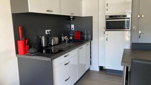 A modern kitchen with white cabinets, a black countertop, and stainless steel appliances including a stove and oven. - Seaside apartment – Perros-Guirec (Perros-Guirec)