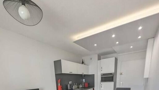A modern living room with a black sofa, red cushions, a wooden TV stand, and a kitchen in the background. - Seaside apartment – Perros-Guirec (Perros-Guirec)