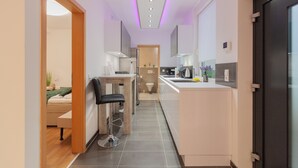 Eine moderne Küche mit einer zentralen Kochinsel, einem Essbereich mit einem Stuhl und einem sichtbaren Badezimmer.